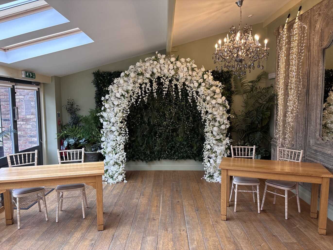 Floral arch against green foliage flower wall backdrop in an elegant venue with chandelier
