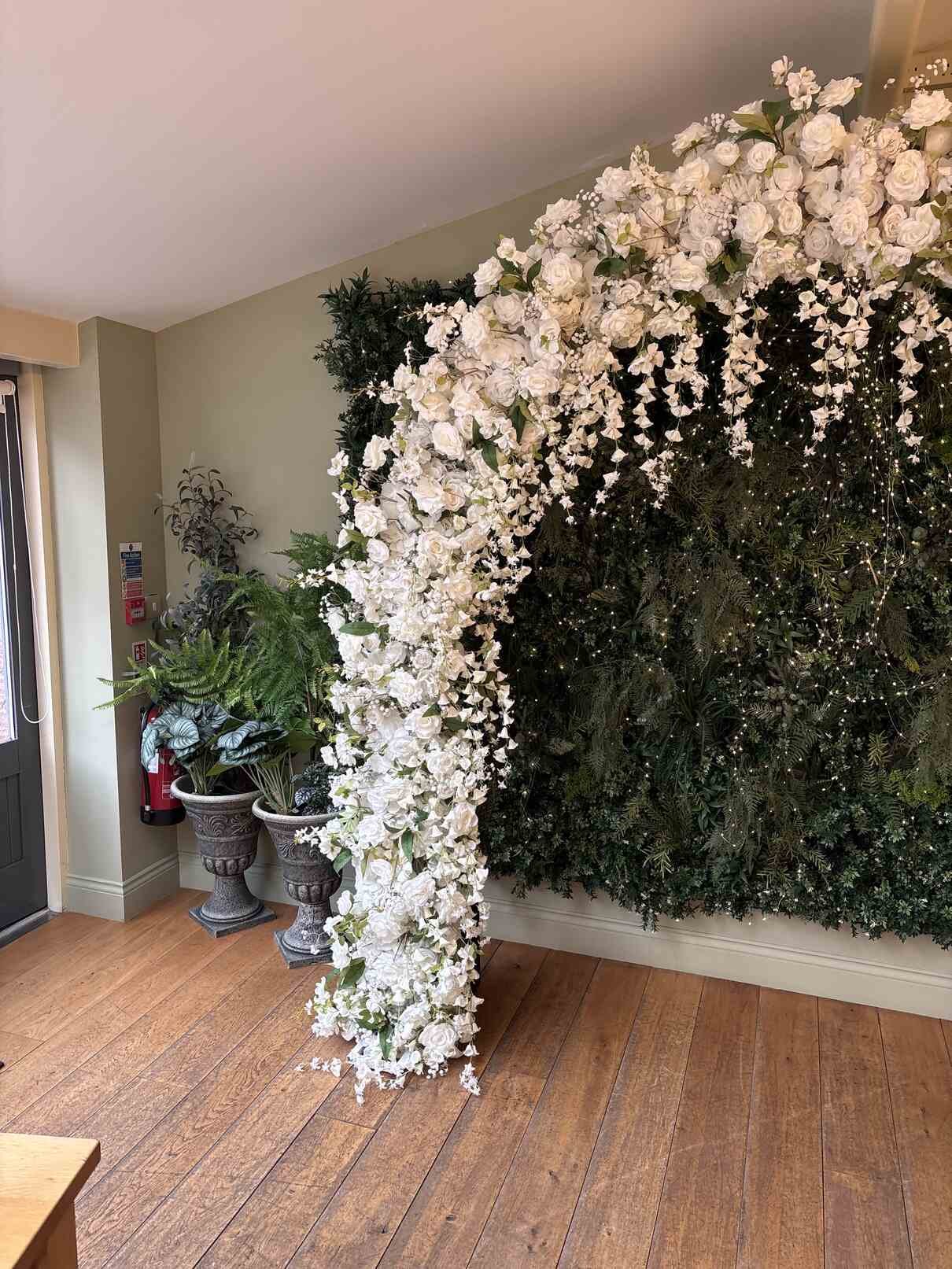 Close-up of white rose floral arch cascading flowers against green foliage wall