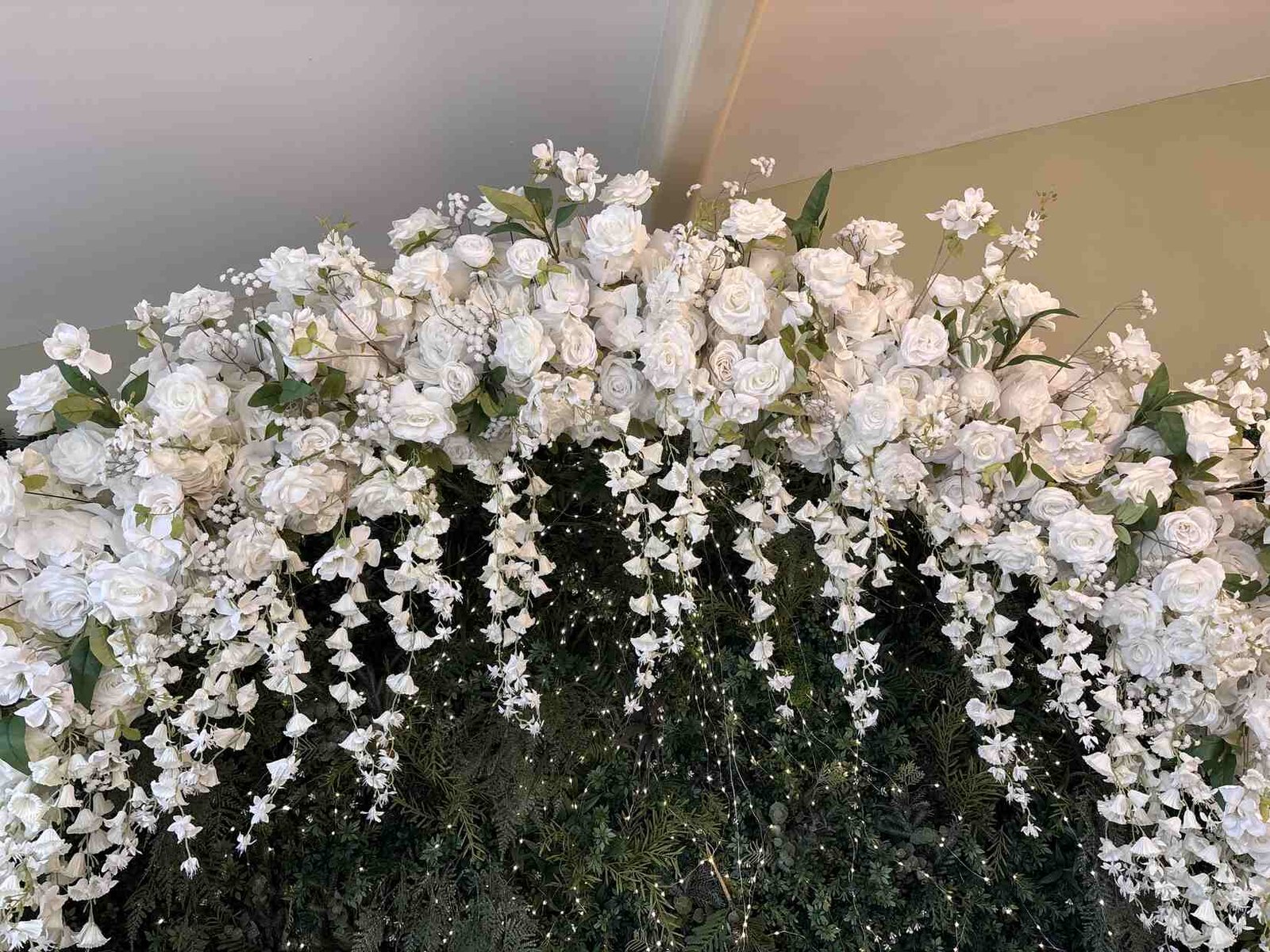 Detail shot of white roses and trailing wisteria on the floral arch with fairy lights